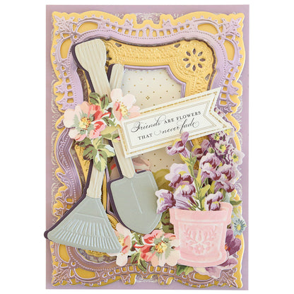 A decorative greeting card featuring Garden Icons Cut and Emboss Folders, flowers, and the phrase "friends are flowers that never fade," adorned with gardening embellishments.