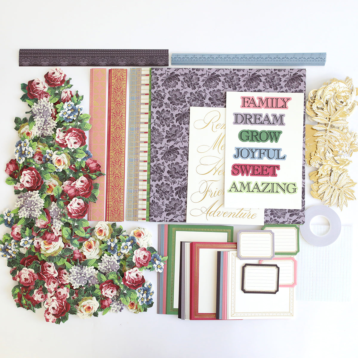 The Simply Astrid Scrapbooking Kit includes assorted scrapbooking supplies such as floral die-cuts, patterned papers, labels, border strips, and word cut-outs featuring phrases like "FAMILY" and "JOYFUL.