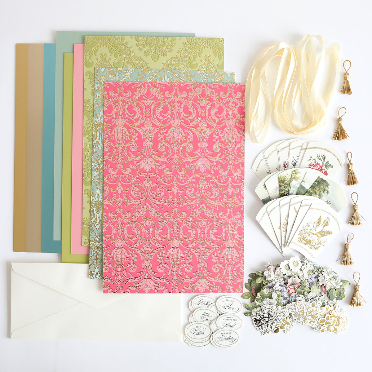 The French Fans Refill Kit beautifully arranged on a white surface, showcasing decorative paper, envelopes, stickers, floral cutouts, ribbon, and tassels.