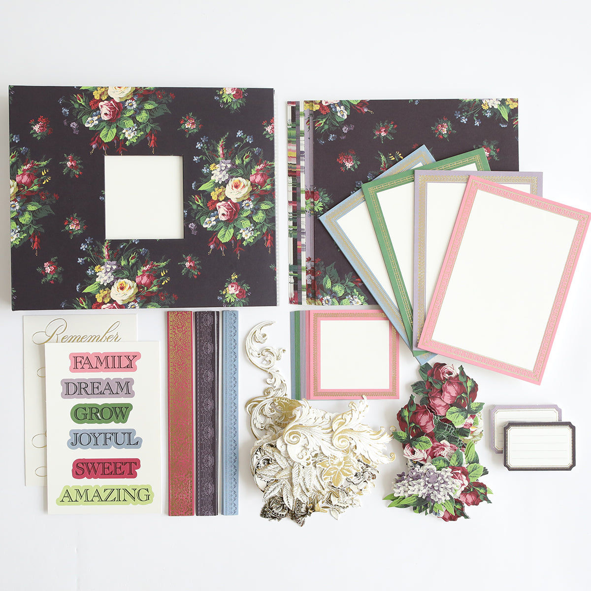 Assorted scrapbooking materials, including patterned paper, frames, floral cutouts, layered word stickers, and decorative elements for your Simply Astrid Mini Album or commemorative photo album are laid out on a white surface.