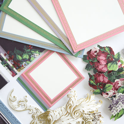 Various stationery items, including ornate paper with decorative borders, floral cutouts, and embossed embellishments, are laid out on a table—perfect for creating a Simply Astrid Mini Album or commemorative photo album.