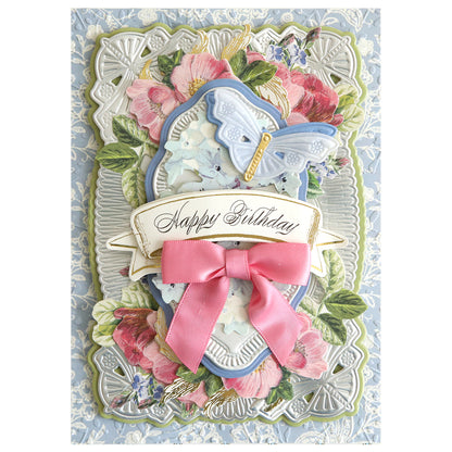 A decorative birthday card featuring floral designs, a pink bow, and a gold "Happy Birthday" banner is adorned with a blue butterfly created using 3D Butterfly Concentric Dies—ideal for card making enthusiasts.