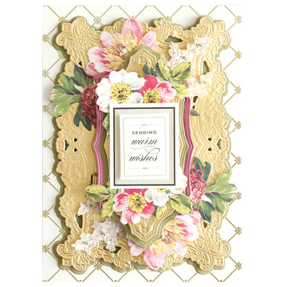 The 3D Filigree Concentric Dies offer an ornate floral greeting card featuring pink and white flowers, intricate gold patterns, and "Sending warm wishes" at the center in a stylish concentric design.
