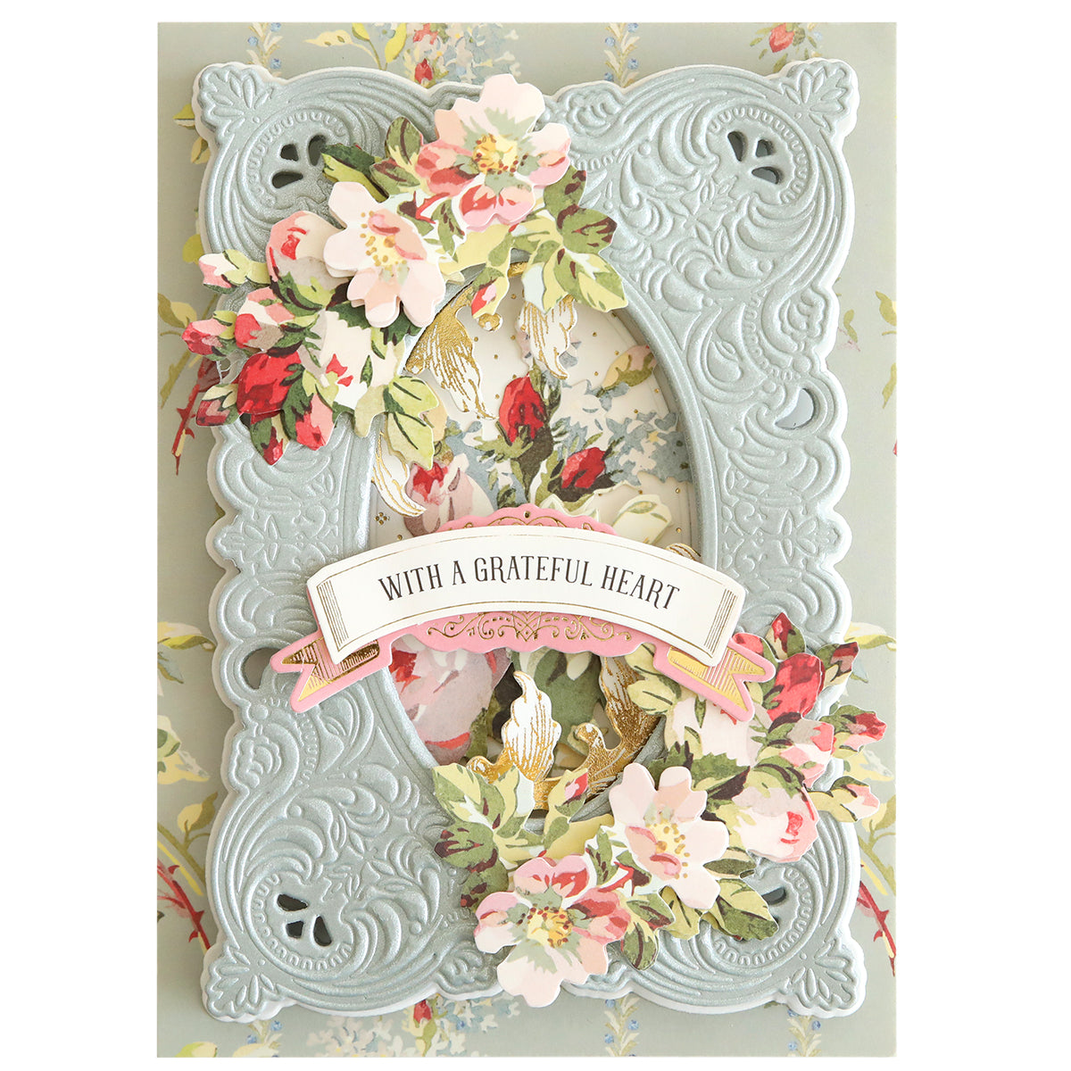 An Autumn Baroque Dies and Ephemera ornate light blue 3D Baroque Concentric Frame die adorned with pink and white flowers surrounds a floral background with a banner reading, “WITH A GRATEFUL HEART.”.