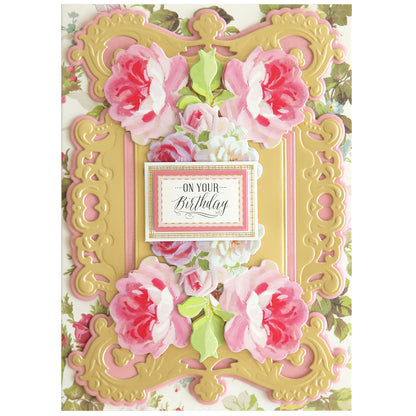 The handmade birthday card showcases a layered design of pink roses and intricate golden patterns. "On Your Birthday" is elegantly displayed in the center, encased by an ornate frame created using Album Frame Dies for added sophistication.