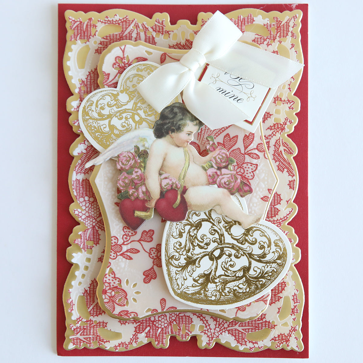 This vintage-style Valentine's card is printed on lace vellum paper from the "Red and White Lace Vellum Papers" collection, featuring a cherub, ornate hearts, and a white bow set against an elegant red and gold background for a charmingly transparent 12" x 12" look.