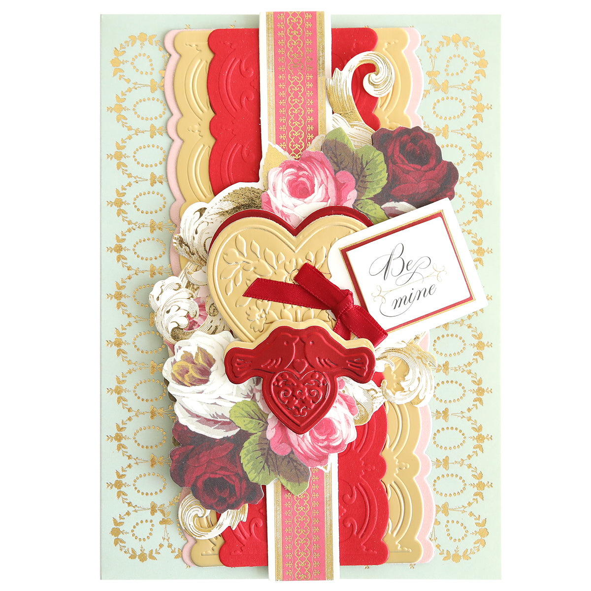 A decorative Valentine's card showcasing Smitten Cut Emboss Folders, with floral accents layered beautifully and adorned with gold embellishments. Featuring a "Be mine" tag, the card displays embossed heart and arrow designs along with striking red and gold heart motifs.