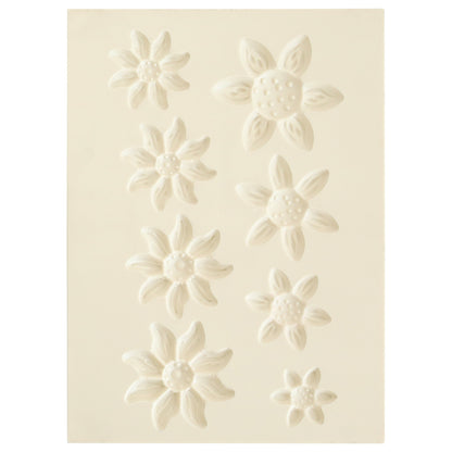 The Blooms Flower Mold, Stamps and Dies set features a white sheet with eight embossed flower shapes in various sizes and petal styles, ideal for crafting dimensional paper flowers using coordinating stamps or the shaping mold.