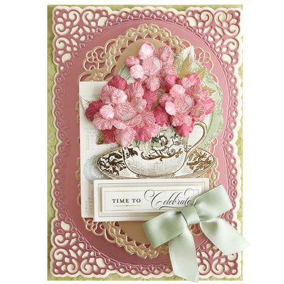 A decorative greeting card with ornate pink and gold borders features a teacup with pink flowers made using the Posies Flower Mold, Stamps and Dies, a "Time to Celebrate" message, and a pale green bow.