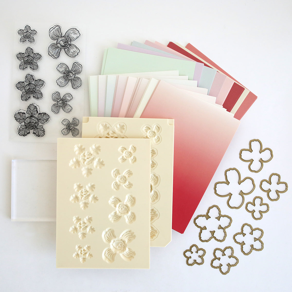 The Posies Flower Mold, Stamps and Dies set includes pastel gradient papers, a flower shaping mold, clear flower stamps and dies, a transparent stamping block, and embossed flower sheets—ideal for paper flower crafting.