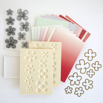 The Posies Flower Mold, Stamps and Dies set includes pastel gradient papers, a flower shaping mold, clear flower stamps and dies, a transparent stamping block, and embossed flower sheets—ideal for paper flower crafting.