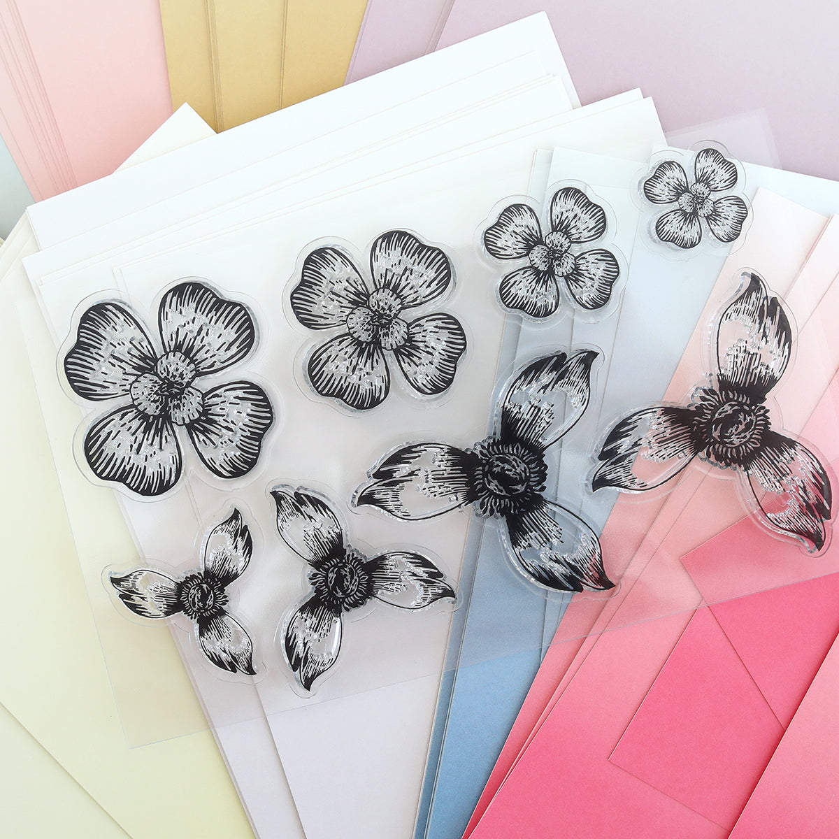 Blossoms Mold, Stamps and Dies features clear plastic sheets with black ink floral stamps on pastel papers, accented by paper flowers in white, yellow, blue, pink, and cream crafted using the included cutting dies.