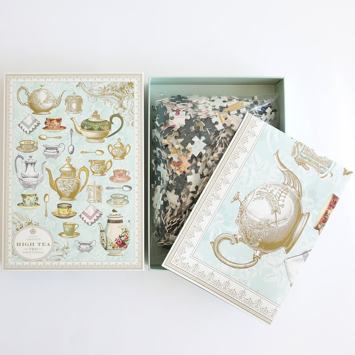 The High Tea Jigsaw Puzzle, ideal for tea and puzzle fans, features charming teapot and cup images. Inside the open box are puzzle pieces ready to be assembled with a helpful guide.