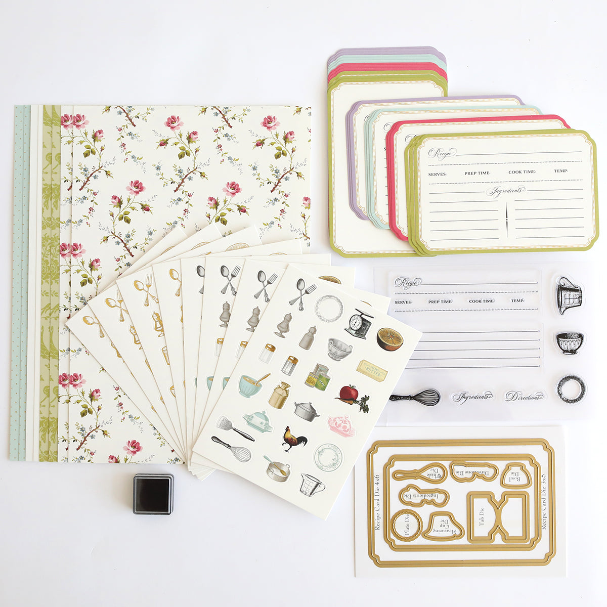 The Recipe Card Stamps, Dies and Embellishments kit includes floral scrapbook paper, recipe cards, decorative stickers, cutting dies, clear stamps, and an ink pad arranged on a white surface.