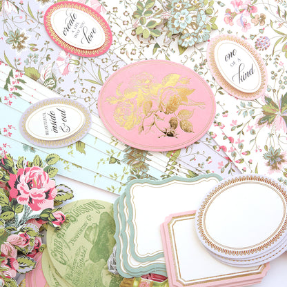 The Mirror Card Craft Box features a floral-themed stationery collection, complete with cards, ornate oval tags adorned with phrases, all set against a floral background enhanced by shimmering foil embellishment stickers.