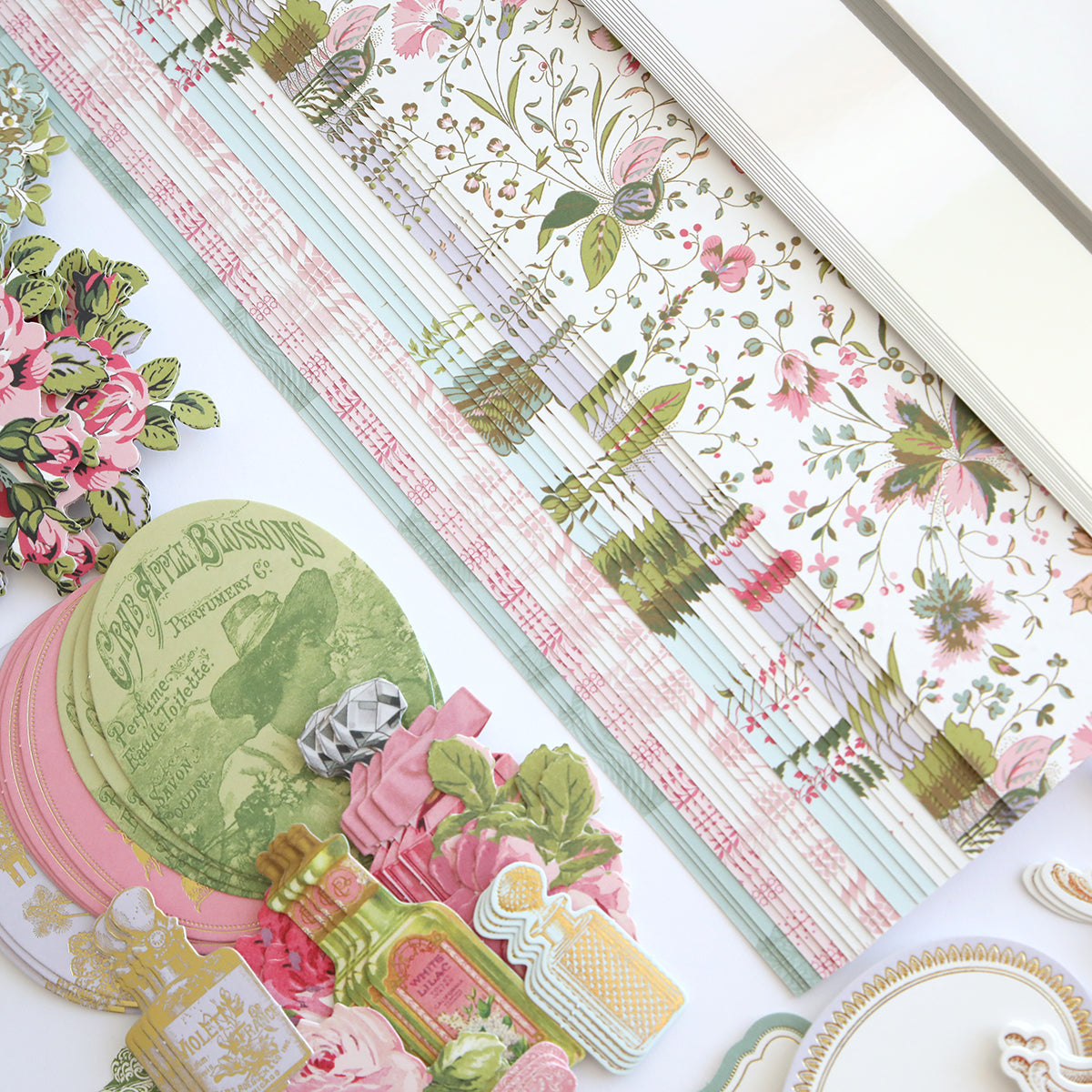 The Mirror Card Craft Box, featuring floral paper, decorative elements, postcards, and foil embellishment stickers, is elegantly arranged on a white surface.