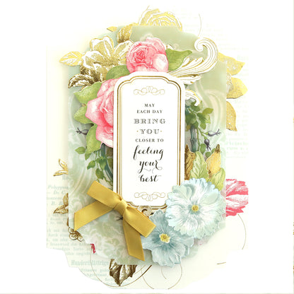 The Simply Get Well Card Making Kit includes a heartfelt card with floral designs, featuring pink roses, a blue flower, and gold accents with a gold ribbon. The text reads: "May each day bring you closer to feeling your best." Includes delicate 3D embellishments for extra charm.