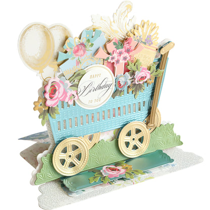 A 3D Wagon Easel Die Set pop-up birthday card features a decorative garden wagon with flowers, gifts, balloons, and a "Happy Birthday to You" sign.