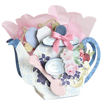 The Teapot Box Dies create a delightful decorative card shaped like a teapot, enhanced with charming paper flowers, teabags, and a spoon. Adorned with floral designs and tied with a gentle pink ribbon, it’s perfect for presenting sweet treats.