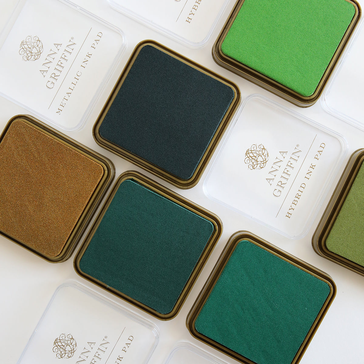 Neatly arranged Anna Griffin Lucky Palette Hybrid Inks in shades of green and gold, with some open lids, offer hybrid and metallic tones to enhance your artistic projects.