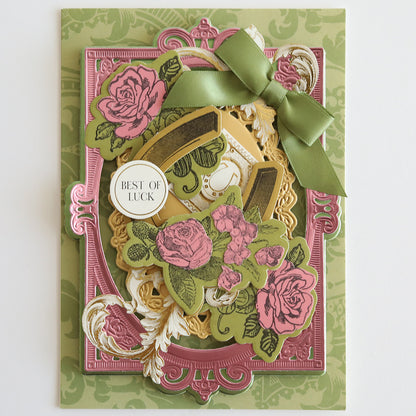 This ornate greeting card features pink roses and a green ribbon, showcasing a "Best of Luck" message on an embossed background. The elegant and charming design is crafted using the Lucky Palette Hybrid Inks for vibrant details.