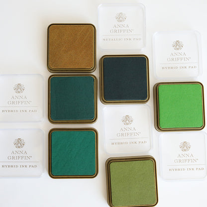 Anna Griffin's Lucky Palette Hybrid Inks include metallic gold, green, and teal shades with transparent covers nearby.