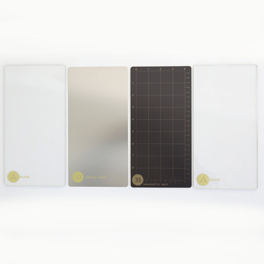 Four rectangular die cutting plates—two clear, one metallic, and one black with a grid—are aligned side by side as the Empress Elite Mini 5" x 10" Full Plate Set from Anna Griffin.