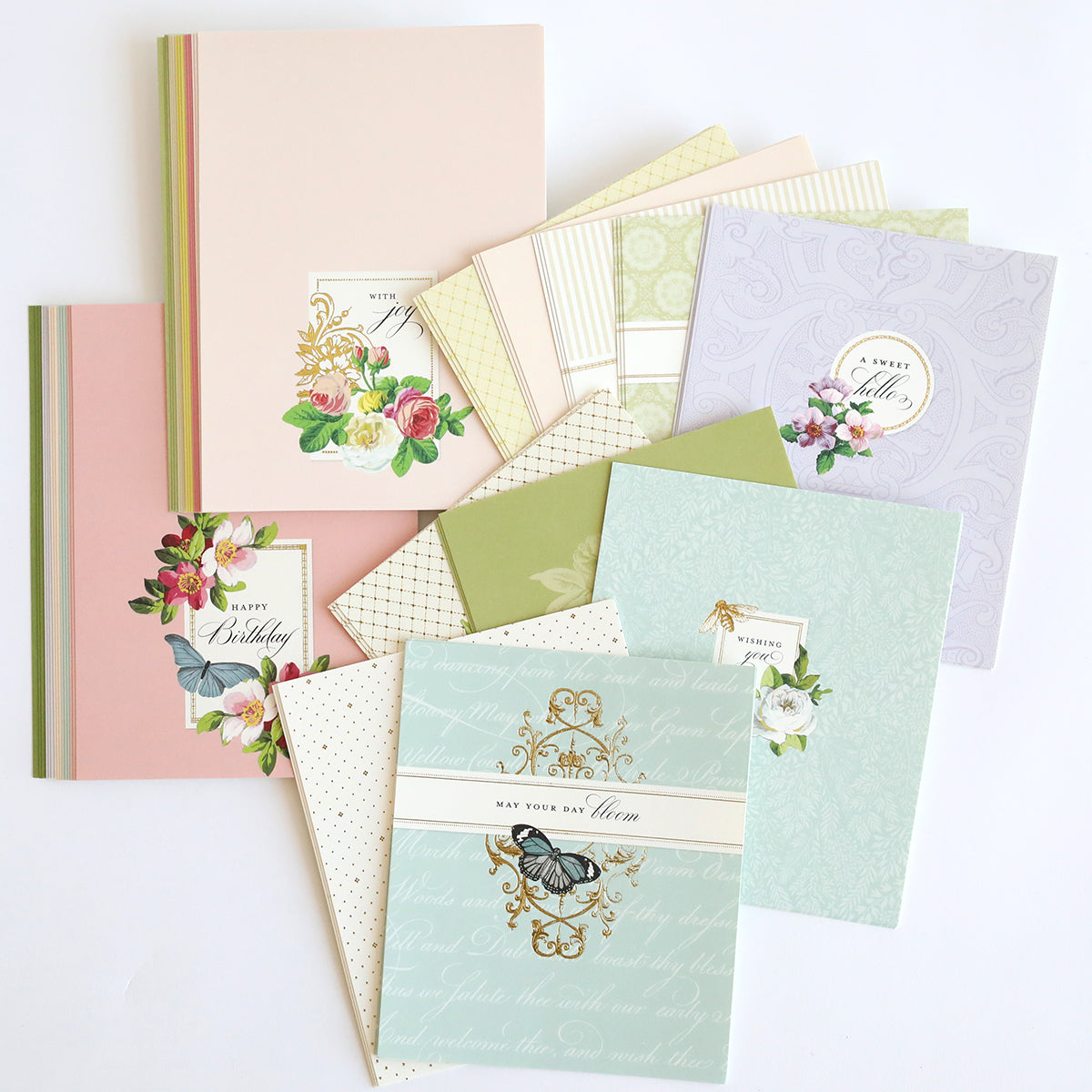 The Clever Sliding Scenes Cards are pastel-themed greeting cards with floral and butterfly designs on high-quality cardstock. Some feature interactive sliding card dies for a playful "Happy Birthday" message.