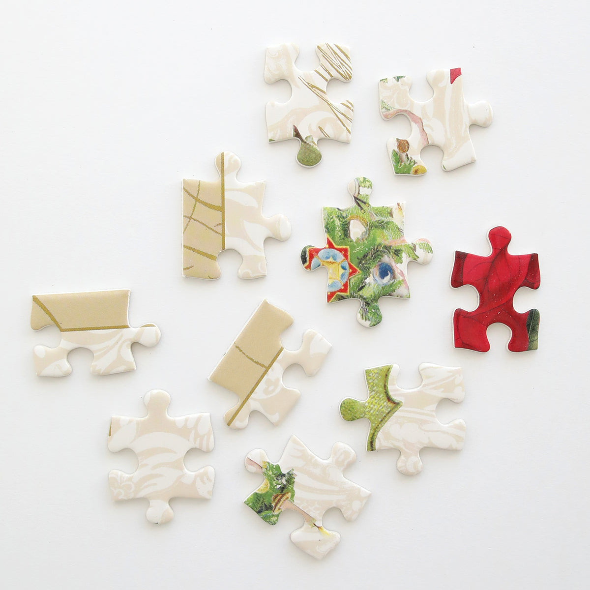 Eleven Christmas Botanicals Jigsaw Puzzle pieces in beige, red, green, and multicolored patterns are scattered on a white background.