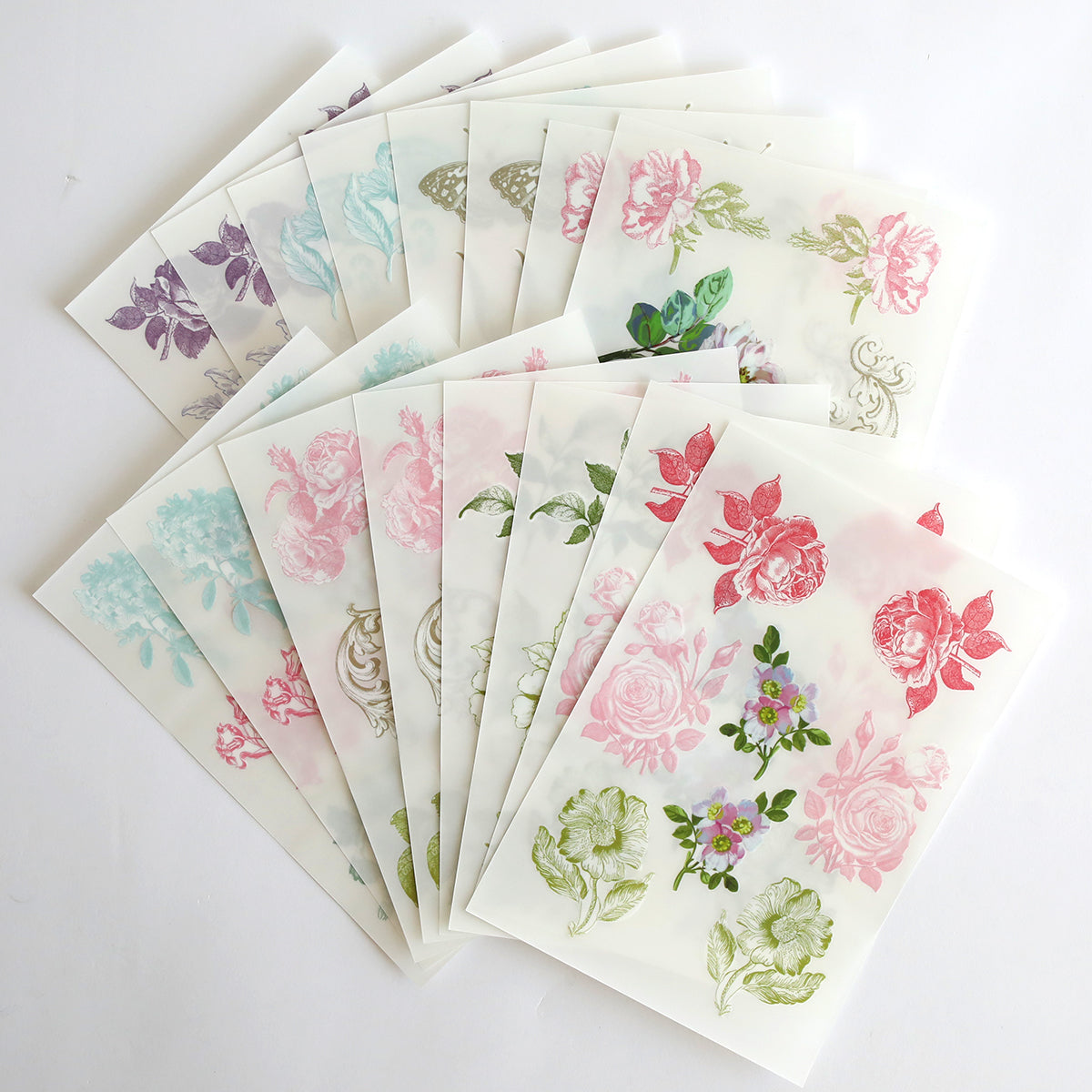 A collection of translucent sheets arranged in a fan shape, each adorned with floral and botanical designs in an array of colors on a white background—ideal for layered card making or enhancing projects with the antique botanical rub on transfers included in the Beautiful Botanical Bundle.