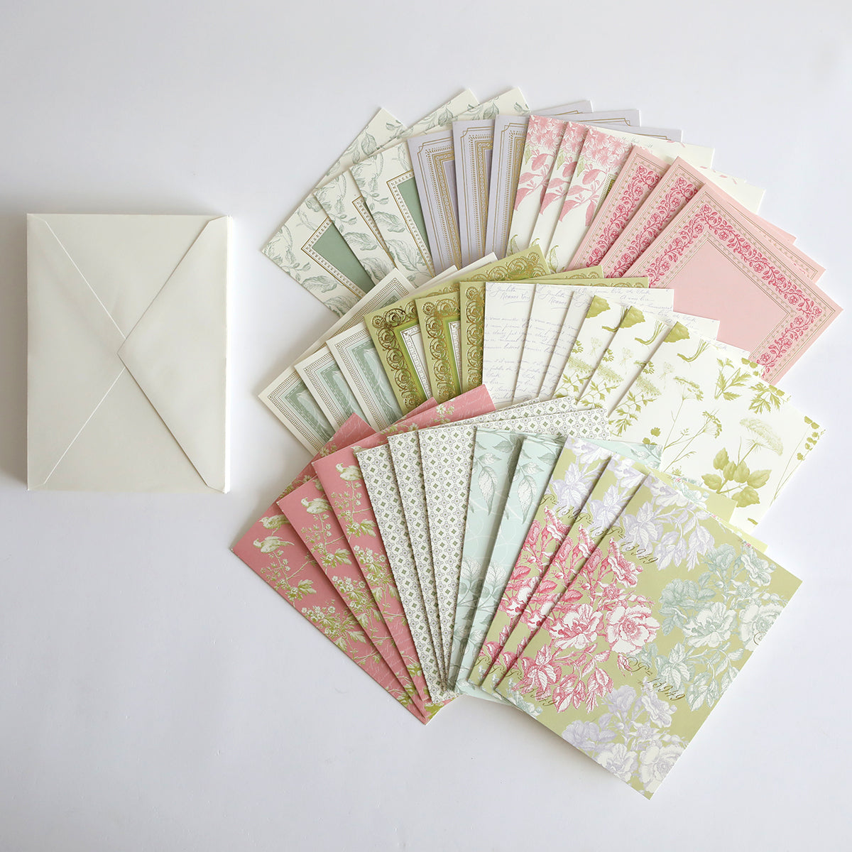 A selection from the Beautiful Botanical Bundle—featuring floral and patterned stationery papers—fans out beside a single cream-colored envelope on a white background, making it ideal for layered card making or pairing with antique botanical rub on transfers.