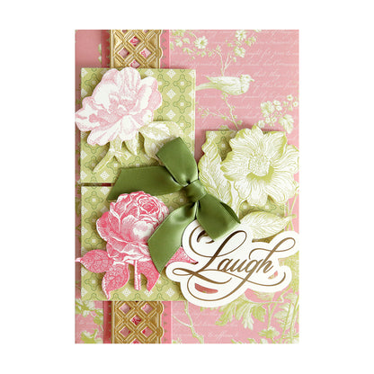 A decorative greeting card from the Beautiful Botanical Bundle, crafted with layered card-making techniques and embellished with pink, green, and gold floral designs, a green ribbon bow, and the word “Laugh” elegantly scripted on the front.