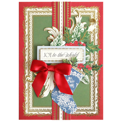 Create festive handmade cards with the Christmas Present Card Making Kit, featuring a decorative holiday card with gold and green borders, a red ribbon bow, blue stocking, holly leaves, and "Joy to the World" text.