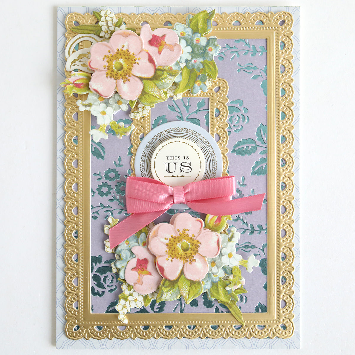 Decorative greeting card featuring pink flowers, gold foil lace borders, a pink bow, and a "This Is Us" label on a patterned lavender background made with Color Drenched Cardstock French Blue—perfect for card making enthusiasts.