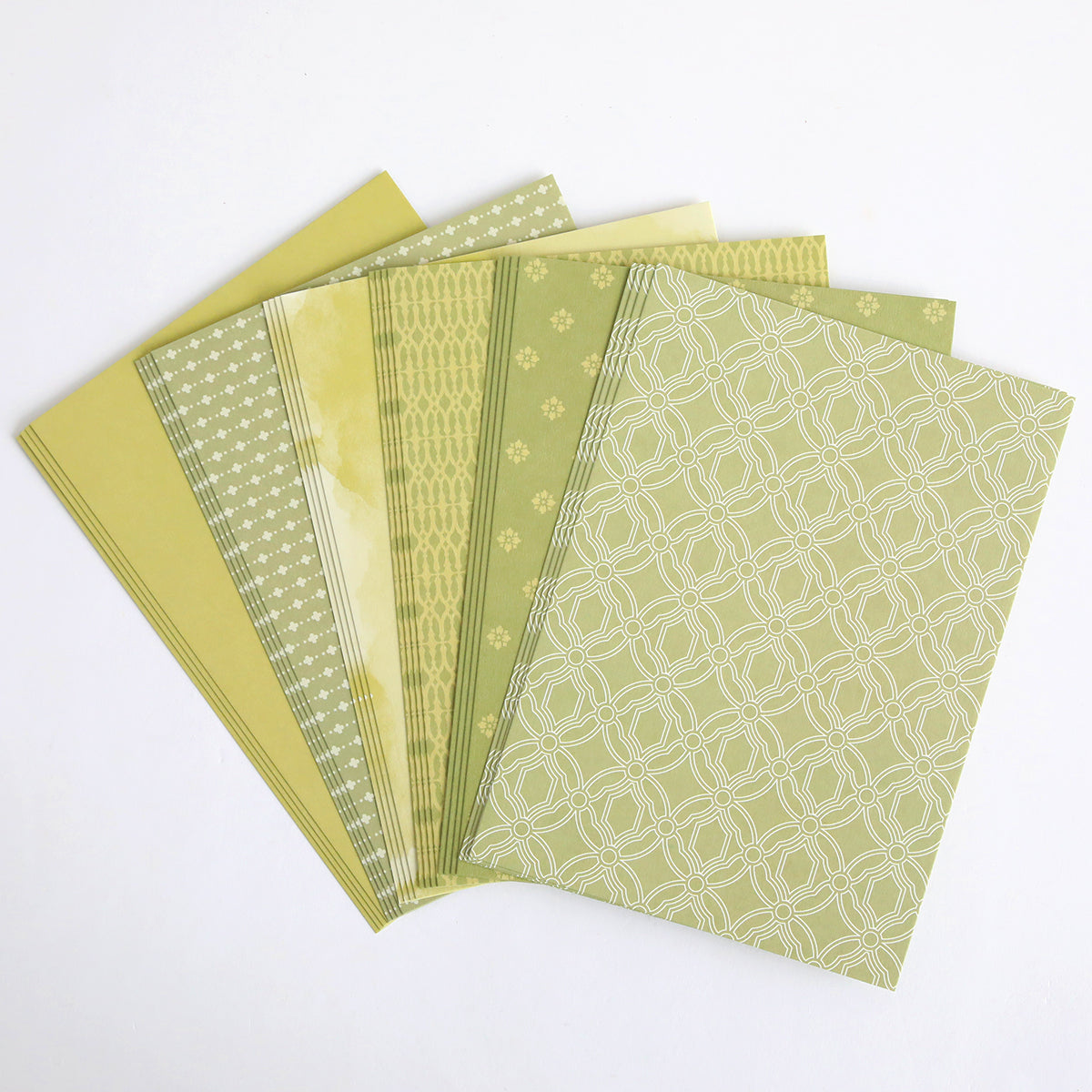 A set of six Color Drenched Cardstock Sage Green papers, featuring assorted green and yellow geometric and floral designs, fanned out on a white background—ideal for card making.