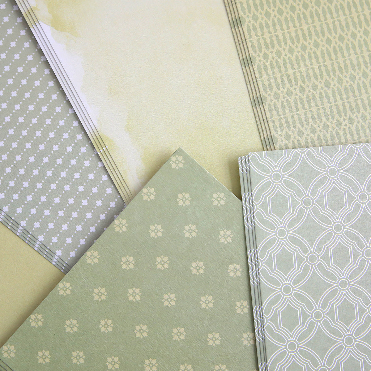 The Color Drenched Cardstock Sage Green, with its geometric and floral patterns in green and beige, is arranged on a flat surface—perfect for card making or pairing with hot foil plates.