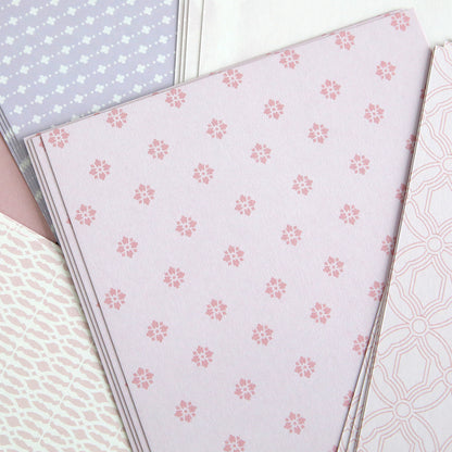 Stacks of pastel-patterned paper with pink floral and geometric designs overlap, perfect for card making. Ideal for use with Color Drenched Cardstock Fresh Lilac and hot foil plates.