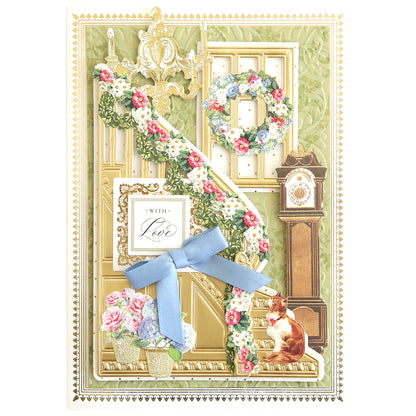 Greeting card crafted with the Grand Staircase Dies and Embellishments, showcasing a gold-trimmed staircase decorated with garland, delicate flowers, a grandfather clock, an elegant chandelier, a cat, floral vases, a wreath, and finished with a "With Love" sign tied with a blue ribbon.