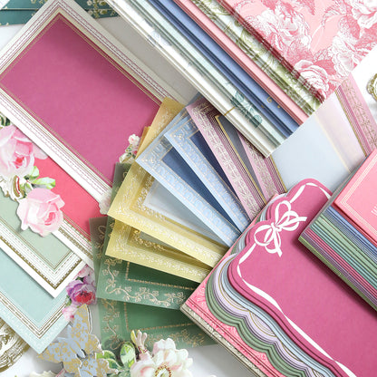 The Birthday Present Card Making Kit includes a selection of colorful, decorative stationery papers and envelopes arranged in overlapping stacks, featuring ornate borders and floral designs—perfect supplies for crafting beautiful handmade birthday cards.