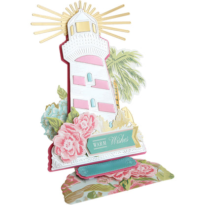 Create an inspirational card using the Lighthouse Easel Die, featuring a pink and white lighthouse, gold sun rays, flowers, and a "Warm Wishes" sign for a decorative touch.