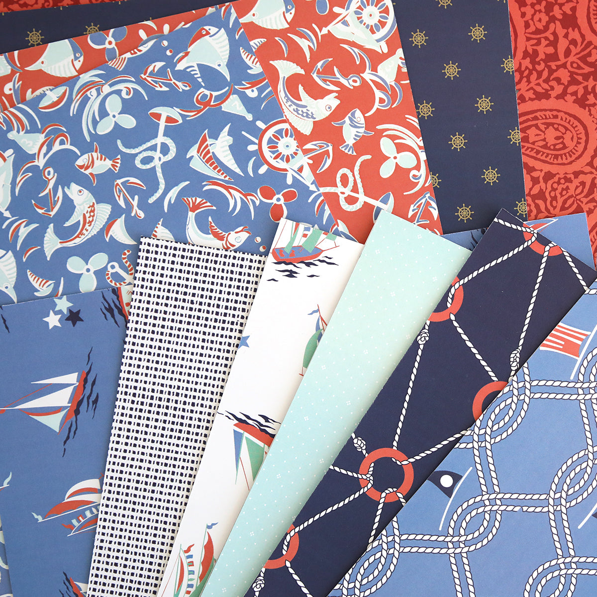 Lighthouse 12x12 Cardstock features double-sided sheets with nautical patterns—ships, anchors, ropes, stars, and geometric prints—in blue, navy, red, and white. Ideal for scrapbooking or pairing with Lighthouse Easel Dies.