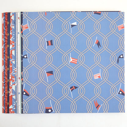 Lighthouse 12x12 Cardstock: Stack of double-sided sheets with coastal designs, featuring nautical motifs like ropes and signal flags in blue, red, and white, arranged side by side on a white background.