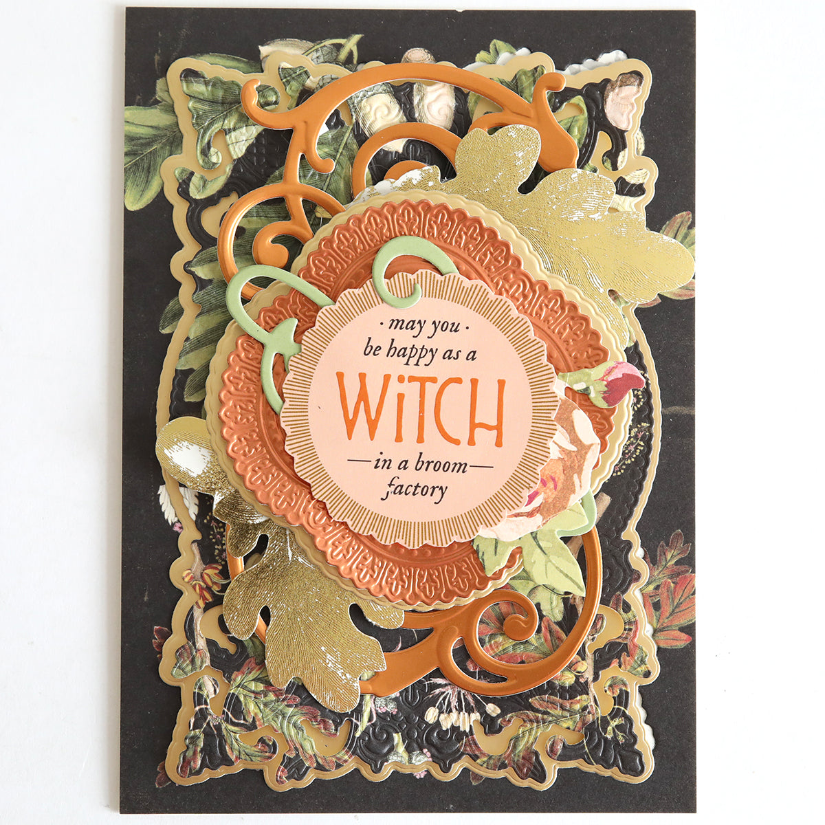 Decorative card featuring gold and orange accents, floral designs, Spellbound Halloween Crafting Pair foil cardstock, and the sentiment “may you be happy as a WITCH in a broom factory.”.