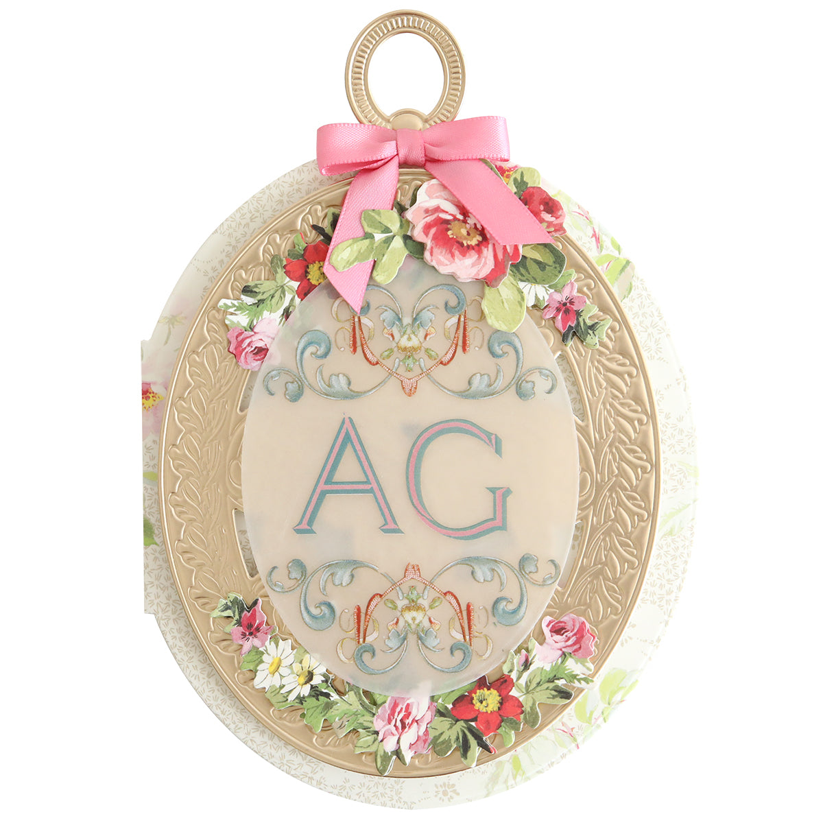 An ornate oval card with embossed gold detail, floral accents, a pink ribbon, and blue "AG" initials on cream—ideal for keepsake cards or pairing with Locket Card Dies to craft elegant, timeless designs.
