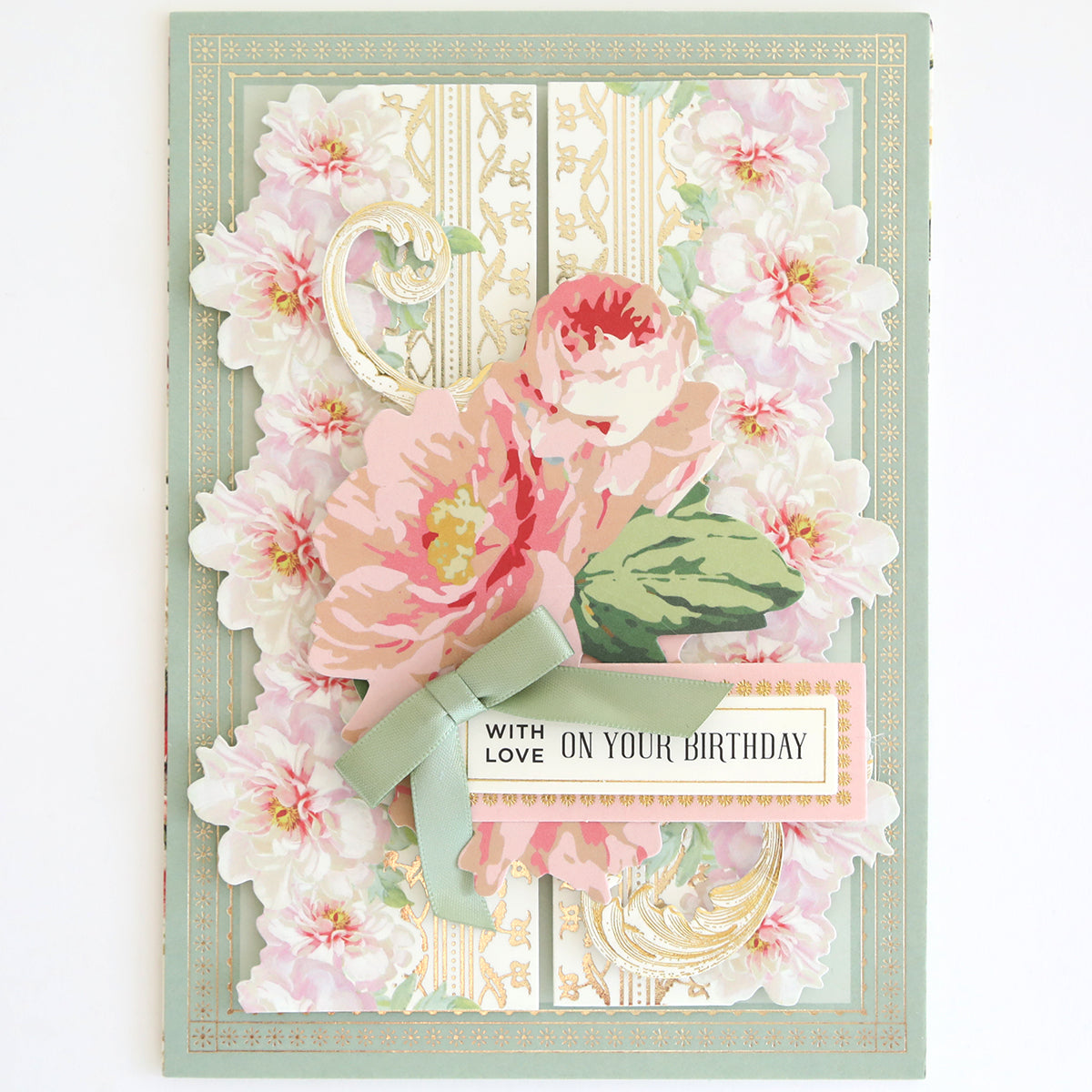 Floral birthday card from the Beautiful Botanical Bundle featuring pink flowers, gold accents, a green ribbon, and a “With love on your birthday” label. This elegant layered card making design is inspired by antique botanical rub on transfers and showcases delicate details.