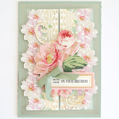 Botanical 12" Border Stickers add charm to greeting cards with layered pink flowers, a green ribbon, gold accents, and the message "With love on your birthday" on a pale patterned background.