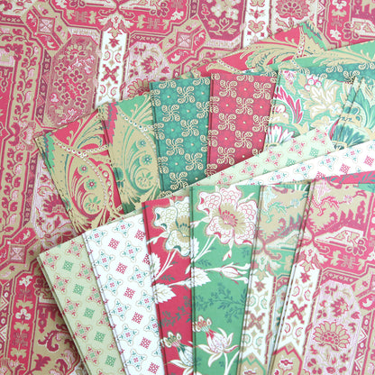 The Jasmine Holiday Cardstock Collection features red, green, and cream sheets arranged in a fan shape on a patterned background—ideal for crafting festive holiday cards.