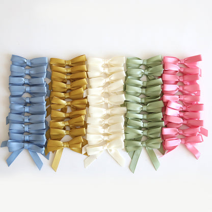 Neatly arranged on a white background, rows of small satin bows in blue, mustard yellow, cream, light green, and pink make the perfect embellishments for handmade cards or for adding a charming touch to 3D Layer Dies with Pre-Tied Bows projects.
