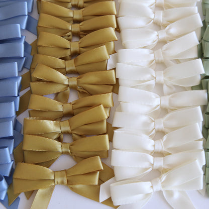 The Perfect Double Bows 50 count features elegant, pre-tied satin bows in blue, gold, and white, neatly arranged side by side as beautiful craft embellishments.