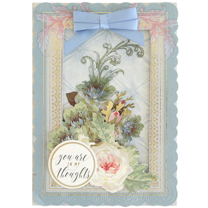 Crafted with the 3D Layer Dies with Pre-Tied Bows, this greeting card features a blue scalloped border, elegant floral design, satin and light blue ribbon bows, and a dimensional round label that reads “you are in my thoughts” in cursive—perfect for fans of handmade cards.